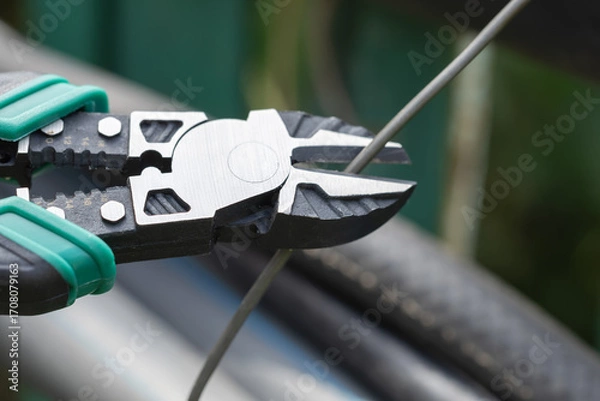 Fototapeta Hands hold nippers, cutting through wires while preparing electrical connections.