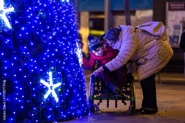 Obraz Caring mother showing christmas tree lights to disabled son in wheelchair