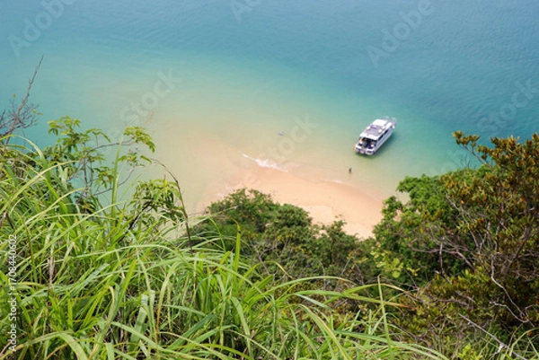 Fototapeta Defocused view through the grass to sandy beach and tourist motor boat on sea island. Background for travel on paradise nature
