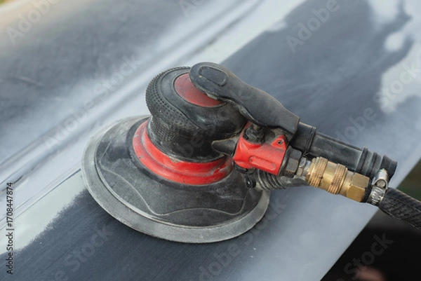 Fototapeta Close-up of an pneumatic orbital sander on a car body panel, used for sanding and surface preparation in automotive repair and restoration. Concept of car repair and auto bodywork.