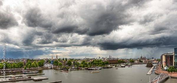 Fototapeta A panoramic view of the Amsterdam city waterfront is dominated by dramatic dark clouds rolling across the sky. 
