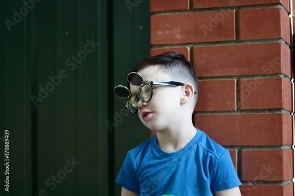 Fototapeta The Image of a little boy beautiful brunette in glasses standing outdoors on a metal door, a conversation with a friend to go walking. Attractive guy, having a conversation