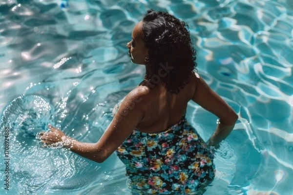 Fototapeta A serene view of a woman immersed in crystal clear pool water, enjoying a peaceful moment with an elegant floral swimsuit that radiates relaxation and joy under the sunlight.