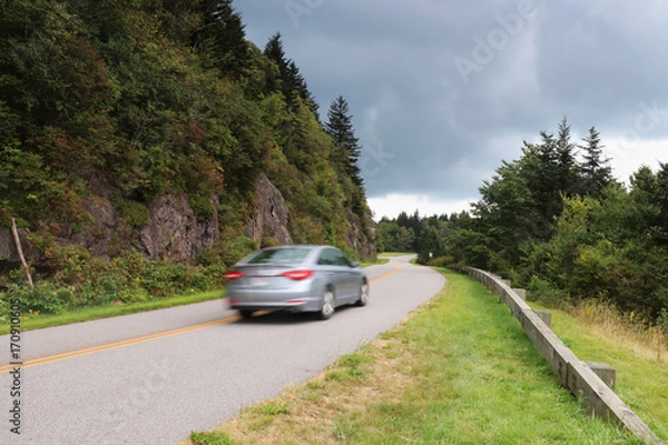 Fototapeta Blue Ridge Parkway scenic view. Summer landscape with cloudy sky over the road with car in motion passing through Great Smoky Mountains scenic highway Blue Ridge Parkway at North Carolina, USA.