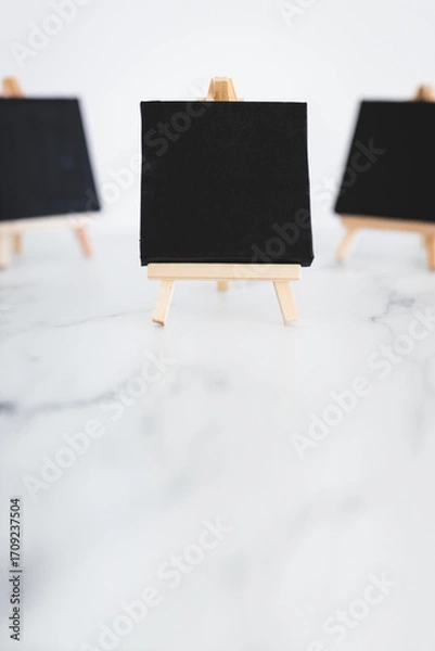 Fototapeta black canvases on miniature easels on white marble, mockup with copy space, shallow dof