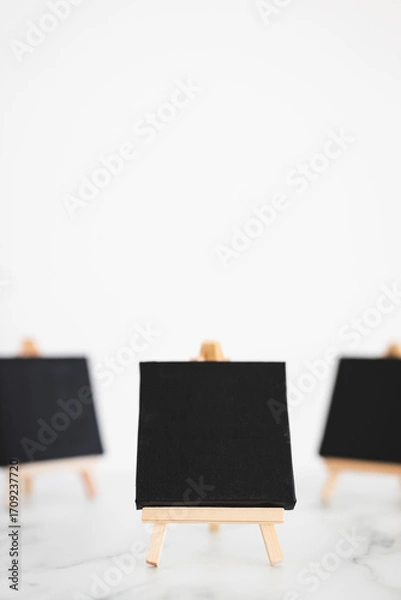 Fototapeta black canvases on miniature easels on white marble, mockup with copy space, shallow dof