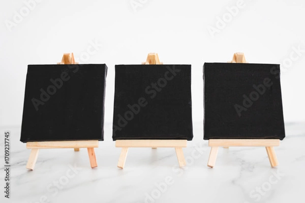 Fototapeta black canvases on miniature easels on white marble, mockup with copy space, shallow dof