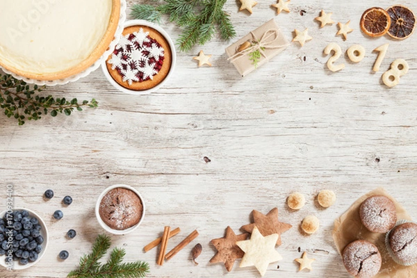 Fototapeta New year preparation concept. Christmass background with berries, cake and gift. New Year composition with snowflakes, sweets, cinnamon, number year 2018 on a beige wooden background.