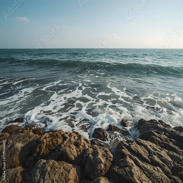 Obraz Foamy waves crash against coastal rocks on a sunny day.