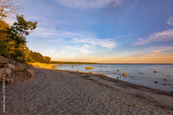 Obraz A stunning sunset over a serene beach in Tiny, Ontario, capturing the tranquil beauty and vibrant colors of the evening sky reflecting on the calm waters.