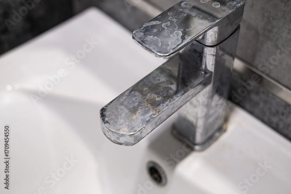 Fototapeta A dirty metal faucet in the sink with limescale, rust marks, and grime around the mixer, showing neglect and the need for cleaning.
