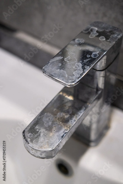 Fototapeta A dirty metal faucet in the sink with limescale, rust marks, and grime around the mixer, showing neglect and the need for cleaning.
