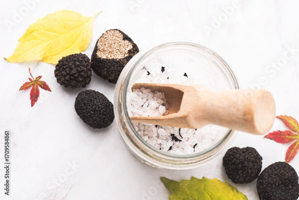 Fototapeta Truffle salt and truffle on the white table with autumn leaves, how to preserve the aroma and taste of black truffle. Preserving black truffle. Delicacy condiment for flavoring dishes