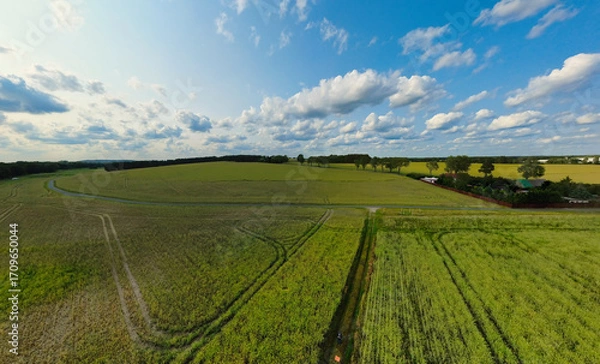 Fototapeta Wide landscape, fields, forests and clouds under a sunny sky in a rural setting.