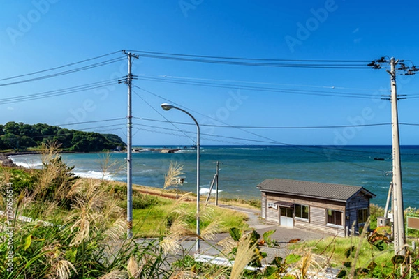 Fototapeta 海辺にたたずむ小さな無人駅舎と日本海の風景。駅舎の看板には漢字で”とどろきえき”と記されている。