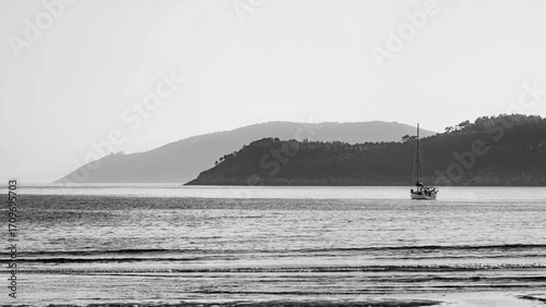 Fototapeta Black and white photograph of a sailboat in the Atlantic with Cape Finisterre and its lighthouse in the background.