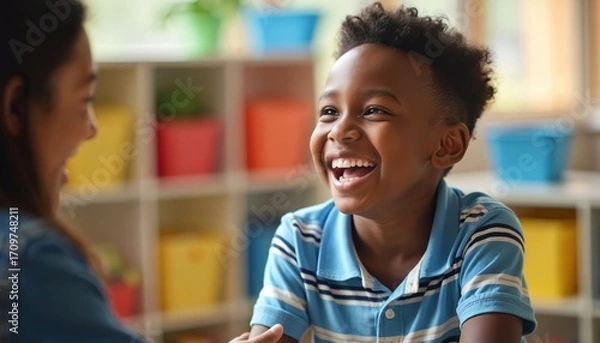 Fototapeta Happy Black boy laughs during autism therapy session with school counselor in supportive, inclusive learning environment. Encouragement, positive growth, understanding central to educational