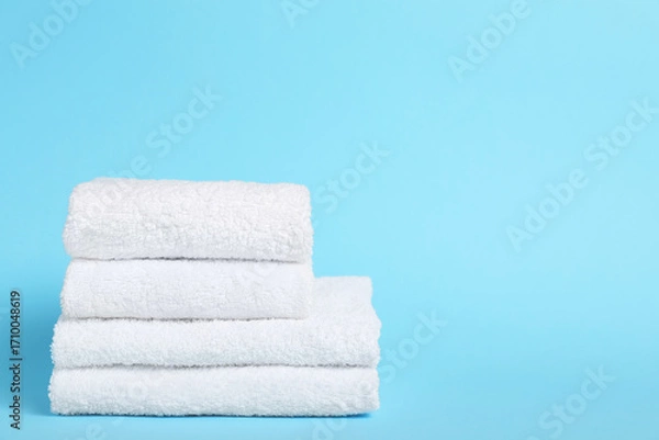 Fototapeta Stack of white towels on light blue background, closeup. Space for text