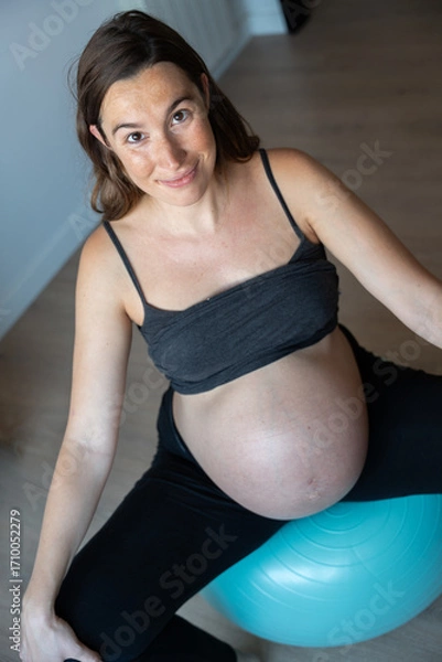 Fototapeta Vertical picture of a pregnant woman doing exercises with pilates ball at home