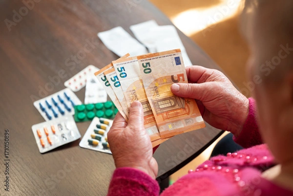 Obraz An elderly woman counting euros near medication. A grandmother counts money against a background of medicines, a symbol of the high cost of medicines and the lack of funds in Europe