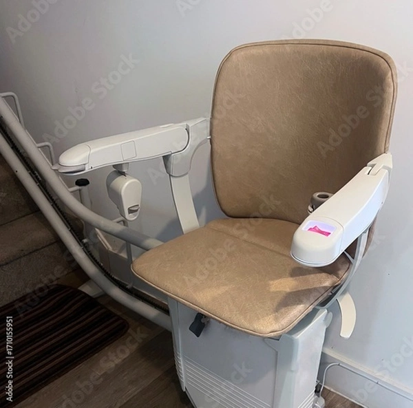 Fototapeta A stair lift or chair lift at the bottom of the stairs in a home. Used to help people with dissabilities, the elderly and those prone to falling to go upstairs and downstairs in their homes.