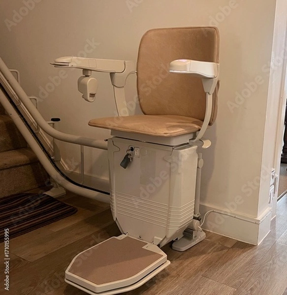 Fototapeta A stair lift or chair lift at the bottom of the stairs in a home. Used to help people with dissabilities, the elderly and those prone to falling to go upstairs and downstairs in their homes.