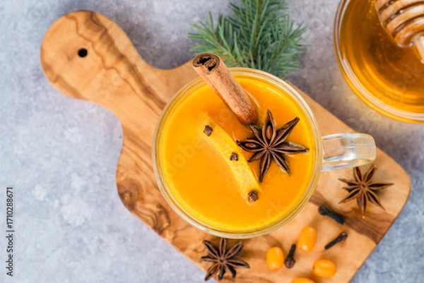 Fototapeta  Close up a cup of sea buckthorn tea with orange, cloves, honey, cinnamon, star anise, honey on a cutting board decorated with Christmas tree branches. Healthy herbal autumn drink well-being. top view