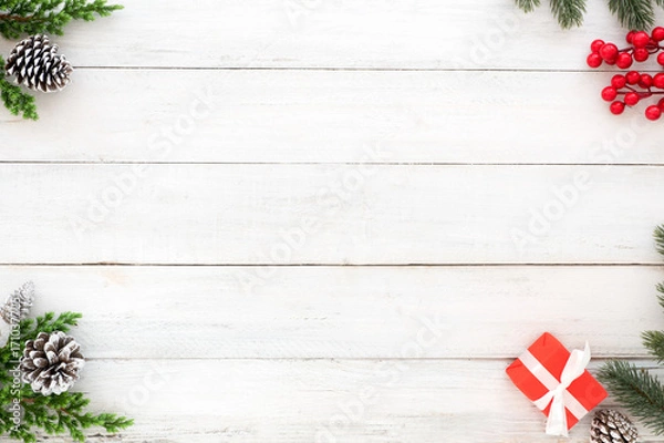 Fototapeta Christmas and New Year background. Christmas frame made of fir leaves, pine cone, gift box, holly berry on white wood background. Creative flat lay, top view design