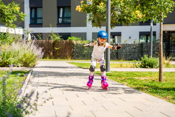 Fototapeta Little girl learning to roller skate for the first time at the age of five. Concept of physical development, balance training and childhood independence through active play.