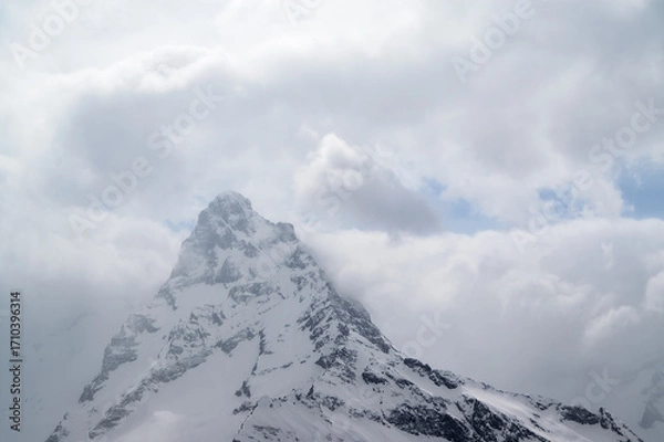 Fototapeta High snowy mountains in fog and cloudy sky at winter