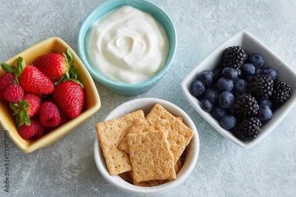 Fototapeta Fresh strawberries, blueberries, blackberries, and yogurt served in colorful bowls with whole grain crackers on a textured surface, showcasing healthy snack options and vibrant colors