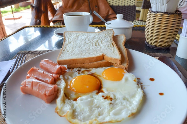 Fototapeta Selective focus of American Breakfast in Hotel in Vietnam, Fried sausages and eggs with toast on white plate.