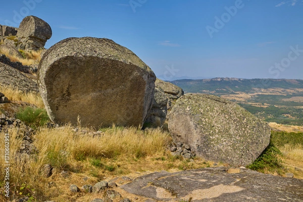 Fototapeta Large granite boulders and dry grass on a hilltop with mountains