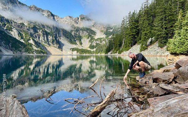 Fototapeta Man kneeling down and touching pristine alpine lake water causing ripples. 