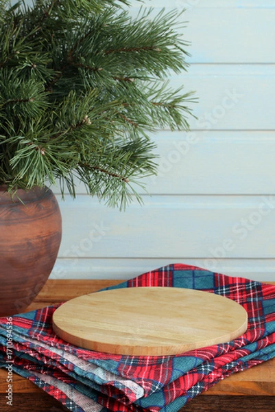 Fototapeta Empty round wooden chopping board on plaid napkin with christmas pine branches in clay pot
