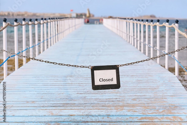 Fototapeta The entrance to the pier is closed by a chain with a sign that says "closed." Wooden pier above the coral reef used for diving,  swimming. Shallow depth of field