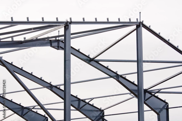 Fototapeta Metal construction, in the photo the structure of the building frame made of metal beams against the background of a gray sky