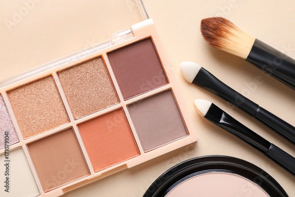 Fototapeta Eyeshadow palette, face powder and makeup brushes on beige background, flat lay