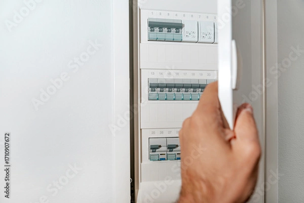 Fototapeta Male hand opening modern electrical panel with circuit breakers inside, safe home power distribution system. Background with copy space.