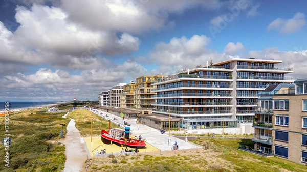 Fototapeta A vibrant, red play boat sits on a sandy playground near a modern residential area by the sea at Kijkduin in The Hague. The scene is bright and inviting, with families enjoying the coastal view.