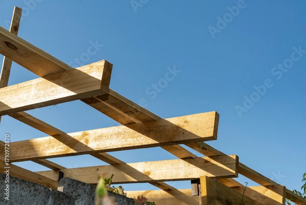 Fototapeta Wooden construction frame with beams against blue sky. Architectural detail and building structure concept.