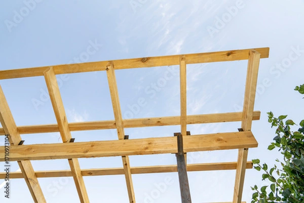 Fototapeta Wooden construction frame with beams against blue sky. Architectural detail and building structure concept.