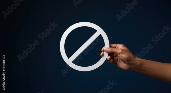 Fototapeta Hand holding a white prohibition sign. Concept of restriction, ban, or no entry. Visual for rules, warning, and forbidden actions on dark background.
