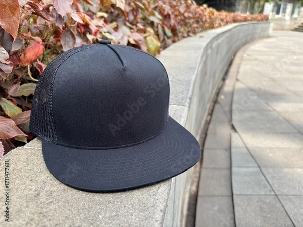 Fototapeta Black trucker cap on stone surface outdoors with background of red leaves and urban walkway