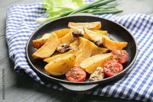 Obraz Frying pan with delicious baked potato wedges on napkin