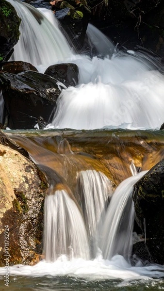 Fototapeta Cascading waterfall over dark rocks