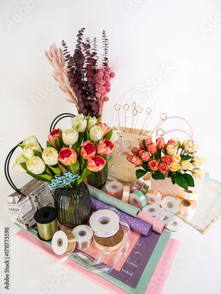Obraz Still life of a set for florists, vases with artificial flowers, paper with flowerpots, multi-colored ribbons and dried flowers on a white background