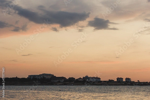 Obraz The city and the sea. On the Sunset. Contour of houses. Clouds over the sea. Evening cityscape. Sky with clouds. Background sky and urban. On the horizon line of the house. Evening. Dusk. Sea town.