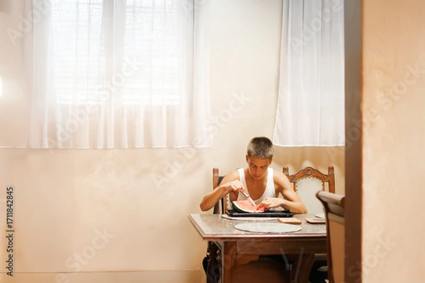 Fototapeta Teenage Boy Eating Fresh Watermelon Indoors During a Healthy Snack Break.