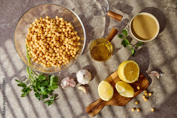 Fototapeta Chickpeas, lemon, tahini and herbs, ingredients for making hummus. Top view.